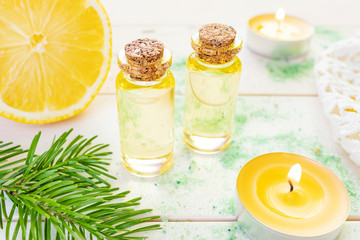 The concept of aromatherapy, relaxation, organics. Transparent bottles with aromatic oil and sea salt, spruce branch, lemon, candles on a light wooden background. Organic Apothecary