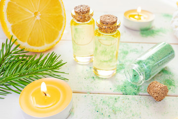 The concept of aromatherapy, relaxation, organics. Transparent bottles with aromatic oil and sea salt, spruce branch, lemon, candles on a light wooden background. Organic Apothecary
