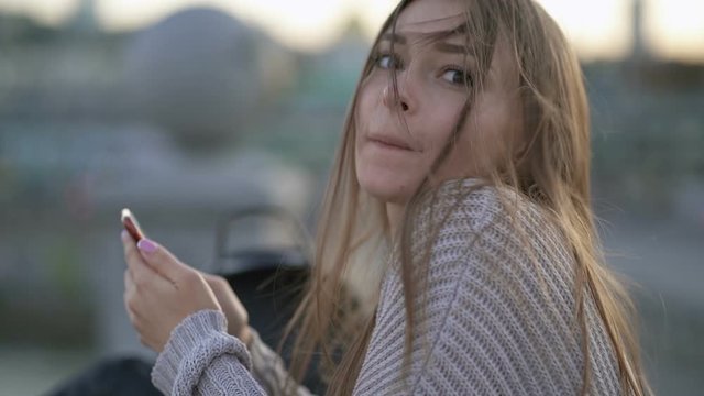 Cute and funny young woman holding smartphone and having fun. Outdoors. Slowmotion.