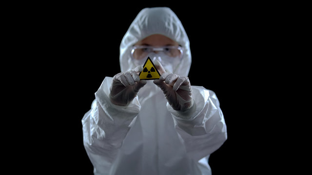 Scientist in protective suit showing ionizing radiation sign, black background