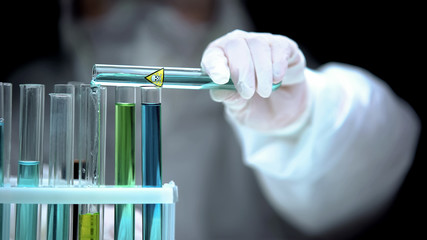 Laboratory worker adding liquid from test tube with poison symbol, life danger