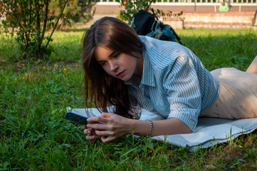smiling young woman touching a mobile phone and lying in a meadow. Concept outdoor recreation with gadgets