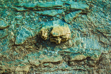 kamienie w zielono niebieskiej wodzie z refleksami światła na powierzchni tafli jeziora
