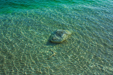 kamienie w zielono niebieskiej wodzie z refleksami światła na powierzchni tafli jeziora