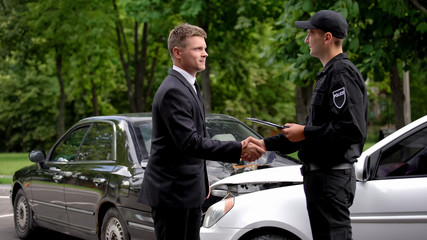 Businessman and policeman shaking hands car accident scene, collision settlement