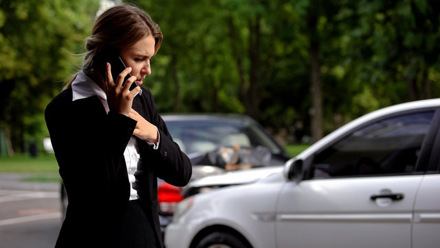 Stressed female driver talking phone car collision scene, auto damage, insurance