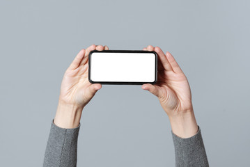 Mobile phone with blank screen in female hands isolated on gray background. Contact us.