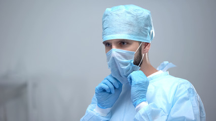 Surgeon wearing medical face mask, preparing for operation, sterility condition