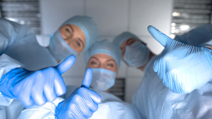 Smiling team of doctors showing thumbs up, pov woman after child birth, hospital - obrazy, fototapety, plakaty