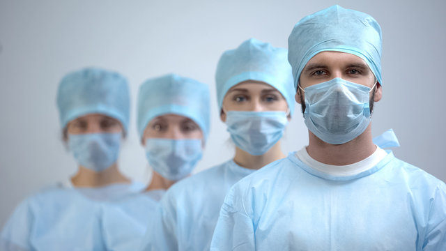 Professional surgeon team in mask and uniform looking at camera, hospital work
