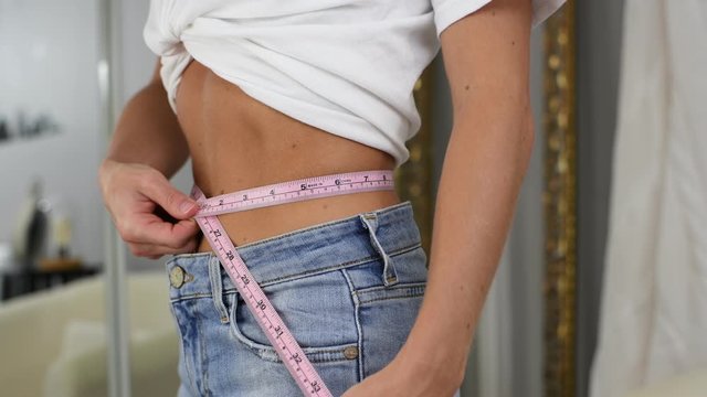 Happy woman in jeans is measuring waist after lost weight.