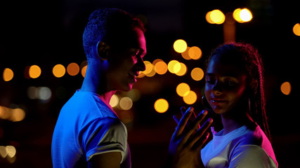 Teenage boy and girl sensually touching hands, romantic date in night lights
