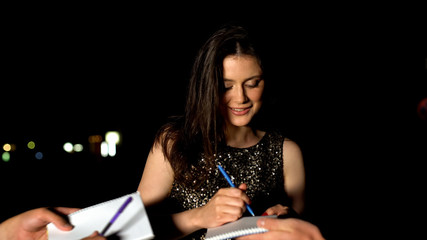 Famous woman signing autographs in fans notebooks at evening party, stars life