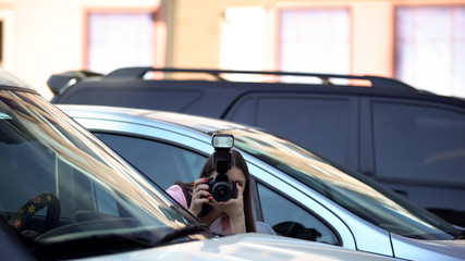 Naklejka premium Female yellow press journalist hiding at parking lot, taking photos, sensation