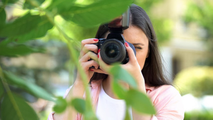Female photographer with professional camera making photos at city park