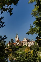 Fototapeta na wymiar Pruhonice, Czech Republic - October 7 2019: Scenic view of famous romantic castle standing on hill surrounded with green trees. Sunny autumn day with bright blue sky. Vertical image.