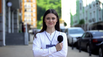 Female journalist with microphone and press pass looking at camera on street