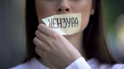 Woman resolutely taking off tape with censored word in russian over mouth