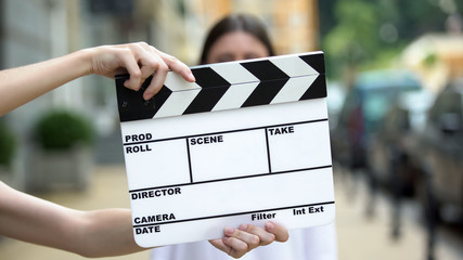 Hands holding clapperboard in front of young woman, movie scene, production