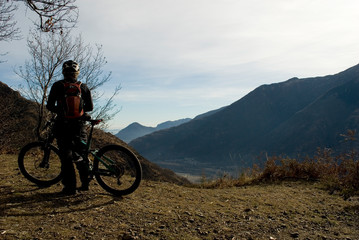 Fototapeta na wymiar man with an electric bicycle, e-bike, ebike, looking mountains covered by the first snow, autumn, sunset, Piedmont, Ossola Valley, Italy