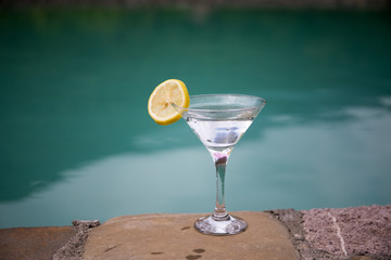 Glass of martini cocktail at swimming pool with ocean and palm tree background. A glass of blue martini cocktail welcome drink bar.Selective focus. season and holidays concept.
