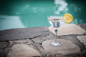 Glass of martini cocktail at swimming pool with ocean and palm tree background. A glass of blue martini cocktail welcome drink bar.Selective focus. season and holidays concept.