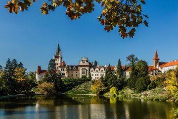 Fototapeta na wymiar Pruhonice, Czech Republic - October 7 2019: Scenic view of famous romantic castle over a lake with its reflection in water. It is standing on hill in a public park. Sunny autumn day with blue sky. 