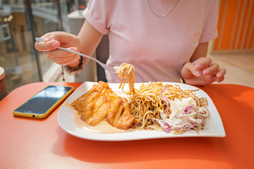 Woman eating fried chicken breast with noodles in restaurant