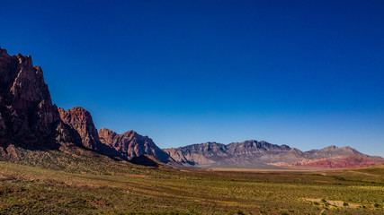 Beautiful view of famous Spring Mountain Ranch State Park near Las Vegas and Red Rock Canyon, Nevada during autumn with pink and red rock mountains, blue sky, green trees and grass, and purple hills