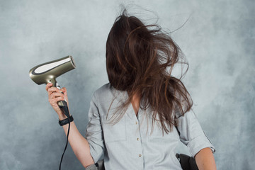 A young woman with long dark hair uses a hair dryer to dry and style. Hairstyle styling and hair care,