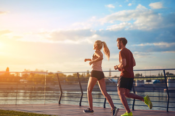 Modern woman and man jogging / exercising in urban surroundings near the river. - obrazy, fototapety, plakaty