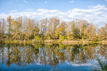 A beautiful view of the river surrounded by trees under blue cloudy sky in fall.