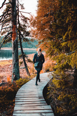 Obraz premium Backview of a adventure blonde active girl walking on a wooden nature path in a beautiful healthy autumn landscape. Oderteich, Harz National Park in the Mountains, Germany