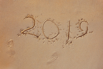 Fototapeta na wymiar Finger inscription on a sandy beach 2019 and foot prints. The outgoing 2019 year. Concept