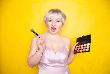 Happy stupid plus size woman having fun with make-up palette set and brush. Professional multicolor...