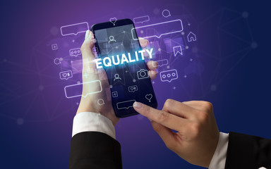 Obraz premium Female hand typing on smartphone with EQUALITY inscription, social media concept