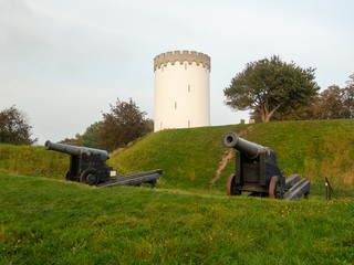 Old white water tower on rampart in city Fredericia, Denmark.Old bronze cannon on rampart in city...