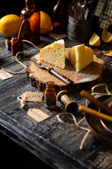 Fototapeta na wymiar homemade two tasty slices of baked lemon biscuit cake with powdered sugar on top stands on wooden board on rustic table with lemons, old bottles opposite concrete wall, selective focus