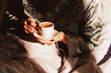 Morning coffee in bed. Female hands holding a cup of coffee in the morning sun. Lazy time