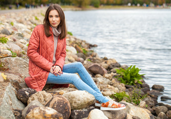 Young stylish woman in a salmon down jacket posing on a background of autumn park