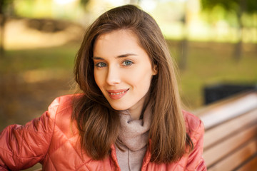Obraz premium Young stylish woman in a salmon down jacket posing on a background of autumn park