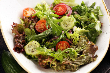 bowl of salad with vegetables and greens, with tomato, cucumber and onions on rustic table