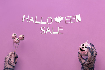 Halloween background in pink, black and white. Top view on paper, text "Halloween sale".  Hands in black mesh gloves with pumpkins painted in metallic pink.