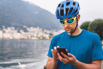 The theme of tourism and travel in Italy. A male cyclist uses a phone on the shore of Lake Como. Tourist guy in a helmet with a bicycle on the shore of a mountain lake in northern Italy