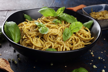 Plate of delicious spaghetti pesto garnished with parmesan cheese and basil on rustic dark background