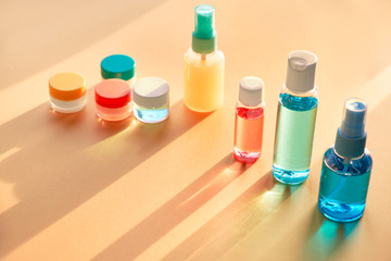 Various cosmetic products in clear plastic travelling bottles on neutral background with long shadows, copy-space