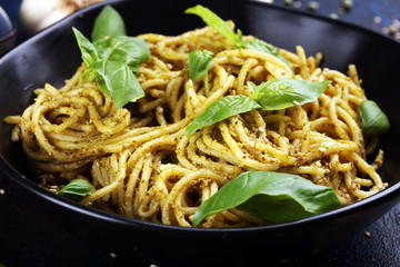Plate of delicious spaghetti pesto garnished with parmesan cheese and basil on rustic dark background