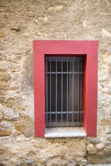 Window in an old stone house with bars and red platbands.