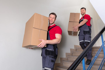 Two Male Movers Walking Downward With Boxes On Staircase