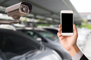 Hand hold mobile phone and CCTV security camera on blue car parking background
